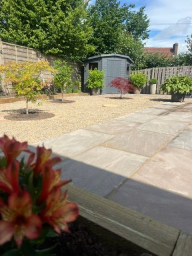 Autumn brown indian sandstone flags, circular flower beds edged with sandstone setts, planted with Japanese maple